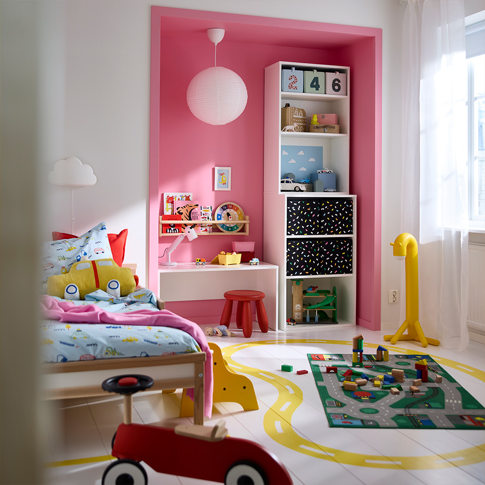 A colourful playroom featuring a LASTARE wardrobe combination with boxes and toys on the shelves, beside a bed and play area.