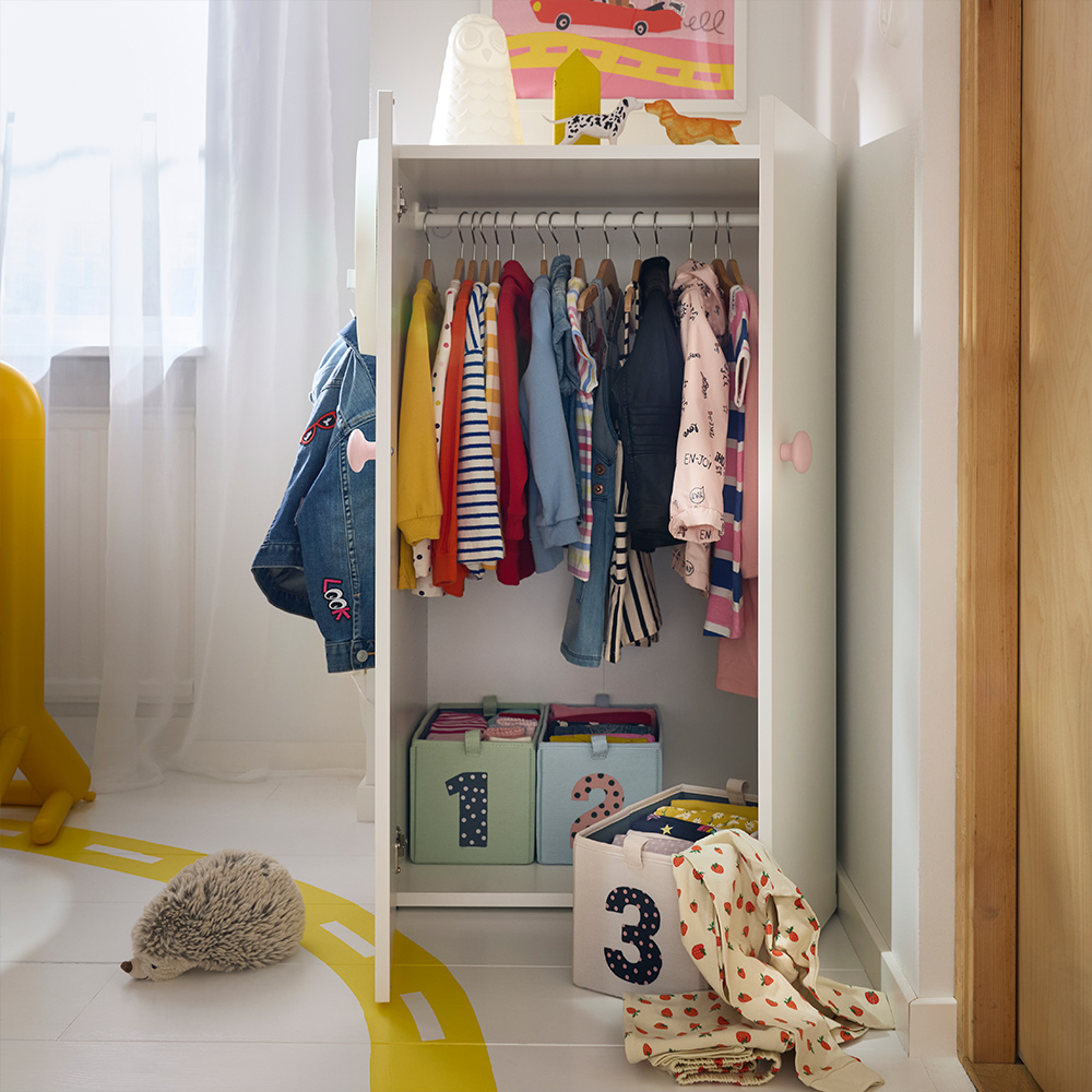 Hanging children’s clothes and labelled storage boxes in a low LASTARE wardrobe combination set in a lightfilled kids’ room.