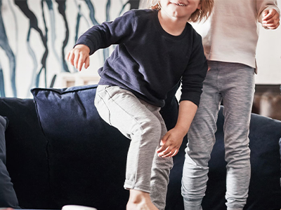 Children playing and jumping on a blue velvet modular sofa with toys nearby.