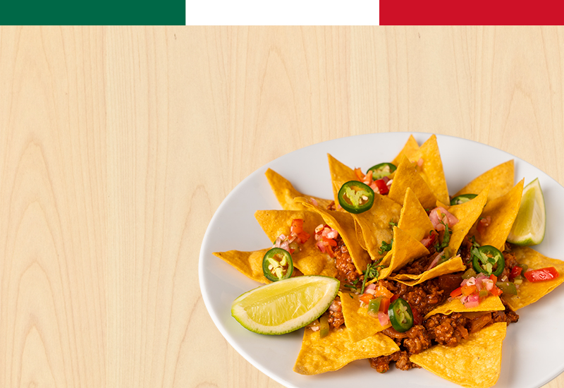Plate of nachos with minced meat, jalapeños, and lime, under a Mexican flag banner.
