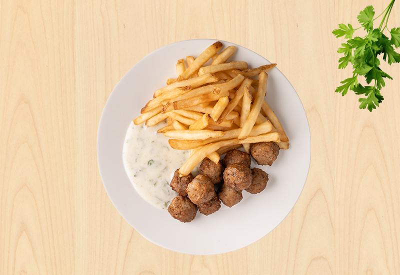 Plate with meatballs, French fries, and yogurt sauce on a light wooden background.
