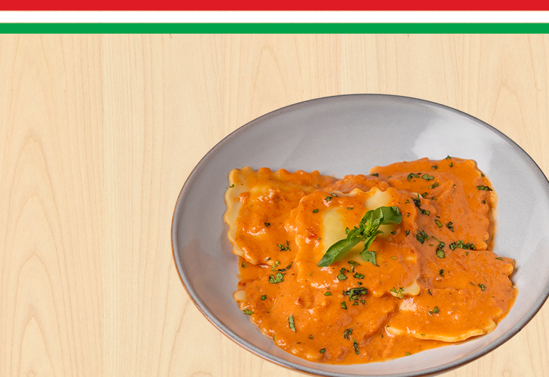 Plato de ravioles con salsa cremosa de tomate, decorado con albahaca fresca.