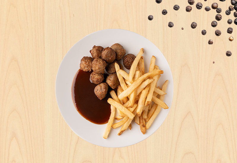 Plato con albóndigas, papas fritas y salsa BBQ sobre fondo de madera clara.