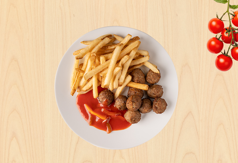 Plato con albóndigas, papas fritas y salsa criolla sobre fondo de madera clara.