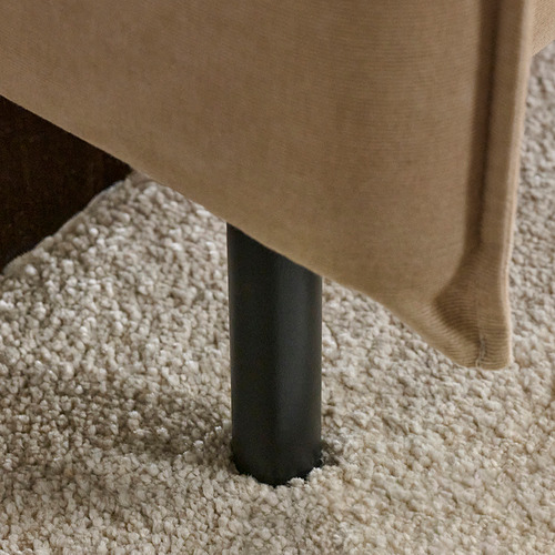 Sofá moderno con patas negras y elegantes sobre una moqueta mullida y texturizada.