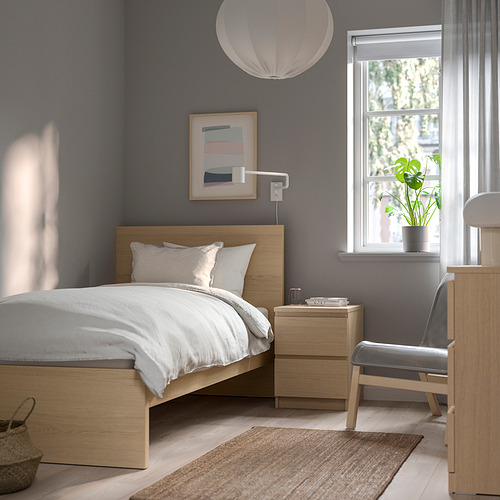 Dormitorio con cama MALM de madera clara, pared gris, mesitas de noche, sillón, lámpara colgante y lona.