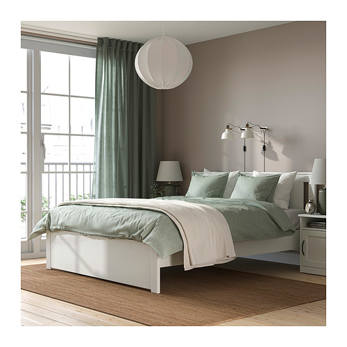 Dormitorio moderno con cama SONGESAND, blanca, elevada, sábanas verdes a juego, suelo de madera, alfombra, gran ventanal, cortinas, lámparas.