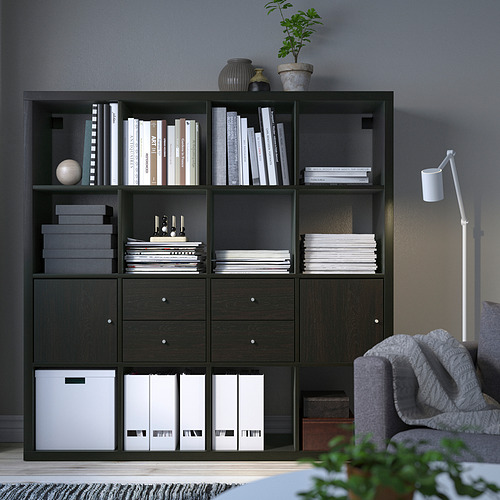 Estantería KALLAX negra con libros, jarrones, plantas, cajas y una lámpara. Diseño alto y moderno.