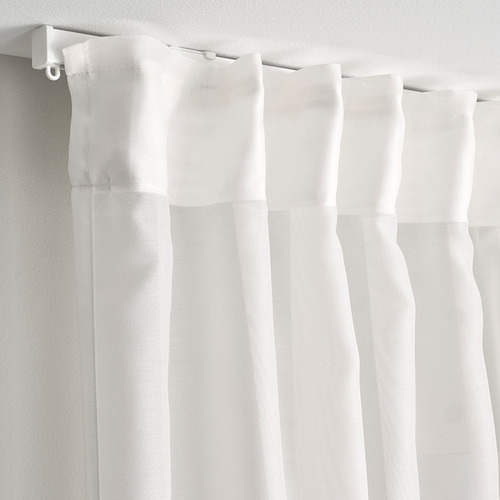 Las cortinas transparentes blancas de STENFRÖ cuelgan de varillas, filtrando la luz solar y ofreciendo privacidad durante el día.