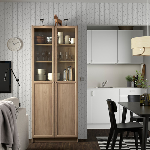 Librería con puertas de cristal en cocina moderna. Caballo de madera arriba, lavabo blanco, sillas negras, reloj de pared, lámpara colgante.