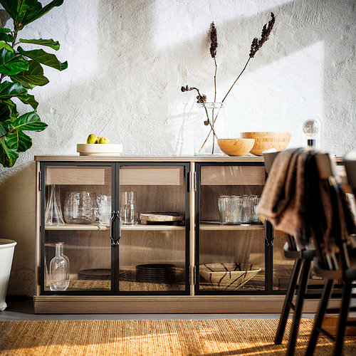 Un moderno armario de madera con puertas de cristal, que exhibe platos, vasos y artículos decorativos.