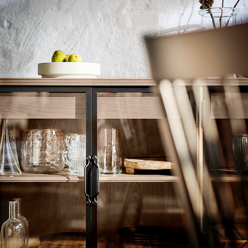 Armario de madera con puertas de cristal para guardar vasos y platos transparentes, un cuenco de manzanas verdes en la parte superior.