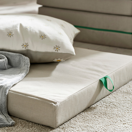 Acogedor colchón infantil en el suelo, de color crema, suave con mango verde y almohada decorativa.