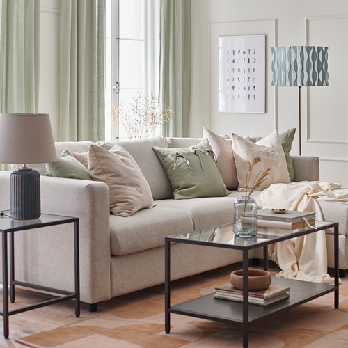 Sala de estar moderna con sofá VIMLE color crema, almohadas verdes, mesa de centro de vidrio con libros, lámpara y arte abstracto.