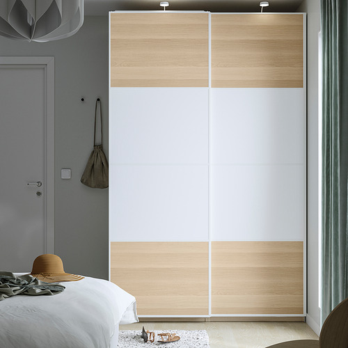 Dormitorio minimalista con closet PAX, madera clara, puertas corredizas blancas. Cama, alfombra pequeña, sombrero beige, bolso.