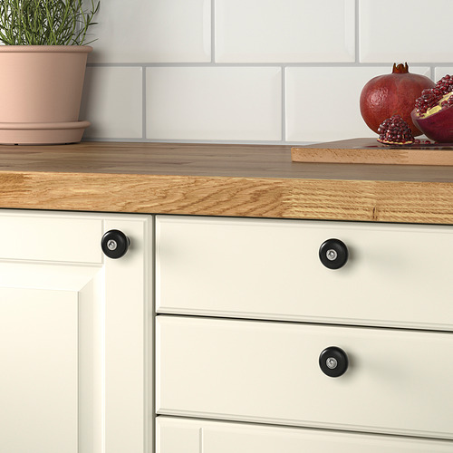 Encimera de madera con mueble blanco, pomos negros mate, granada y planta.