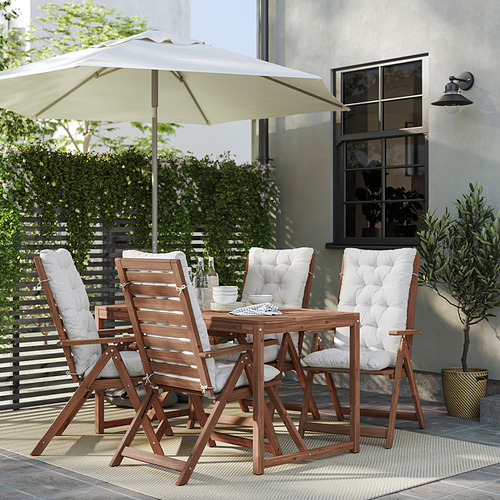 Patio moderno con mesa de madera, cuatro sillas plegables, cojines blancos y una gran sombrilla beige.