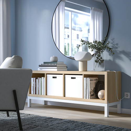Unidad de almacenamiento KALLAX con libros, jarrones y revistas junto a la silla y la ventana.
