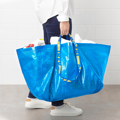 Mujer sosteniendo una bolsa de compras azul de IKEA FRAKTA, que muestra su gran tamaño y asas resistentes.