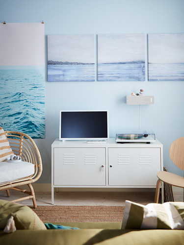 Una habitación de temática costera con un armario metálico blanco de IKEA PS con televisor, silla y paredes azul claro con obras de arte de paisajes marinos.