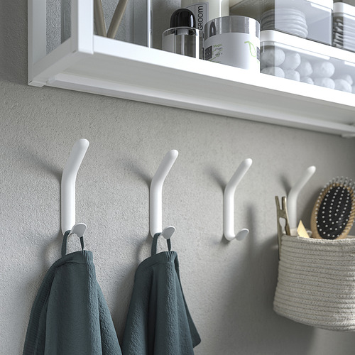Ganchos dobles blancos en la pared con toallas colgadas, estante encima con artículos de baño.