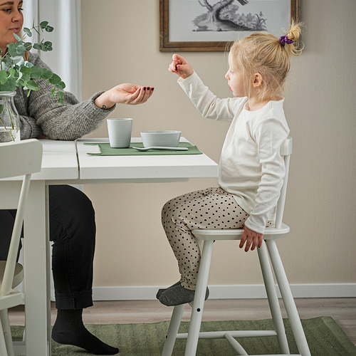 La niña entrega el objeto a la mujer mientras está sentada en la silla de los niños.