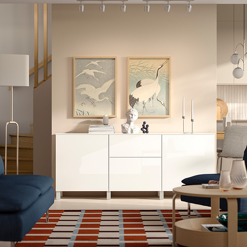 Aparador BESTÅ con pinturas de grúas, alfombra colorida, asientos azules, mesa de madera con libros.