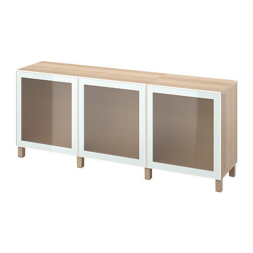 Un aparador BESTÅ de ikea en roble claro y blanco. Tiene tres puertas de cristal y patas de madera.