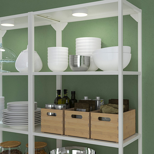 Estantería blanca con cuencos, cajas y vasos. La luz superior ilumina la estantería.