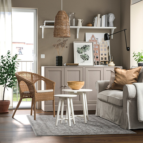 Salón moderno con sofá gris, mesas blancas, sillón de mimbre y decoración de madera. Colores acogedores, bien iluminados, neutros.