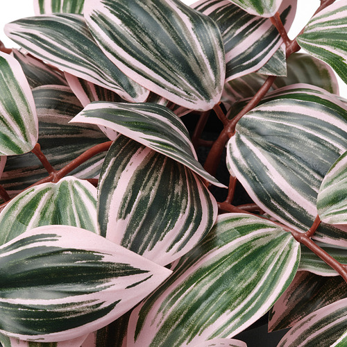 Hojas artificiales con rayas verdes y blancas sobre fondo verde rosáceo, que muestran una artesanía de alta calidad.
