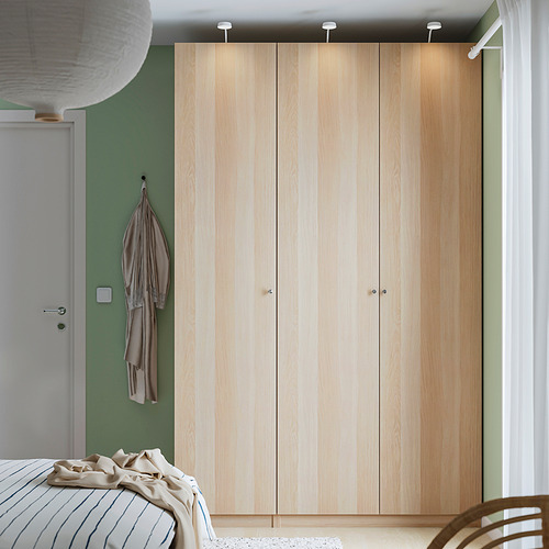 Dormitorio moderno con armario PAX de madera clara, pared verde, puerta blanca, iluminación integrada y cama edredón a rayas.