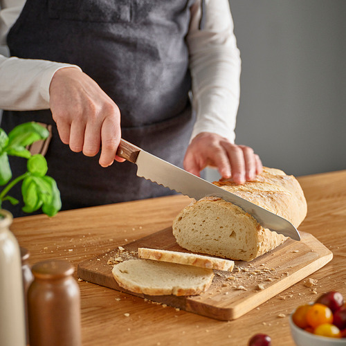 Persona cortando pan con un cuchillo de sierra sobre una tabla de cortar de madera.