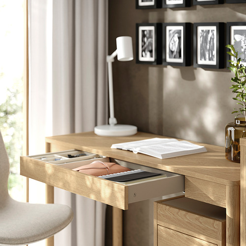Escritorio de madera con cajón abierto, con capacidad para carpetas de archivos, cuadernos. Una lámpara, una planta y marcos de fotos están en la parte superior.