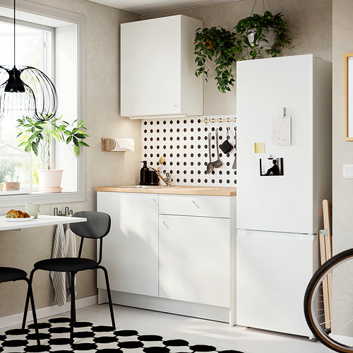 Cocina pequeña y moderna con gabinetes blancos KNOXHULT, detalles negros, encimera de madera marrón, sillas negras y un refrigerador blanco alto.