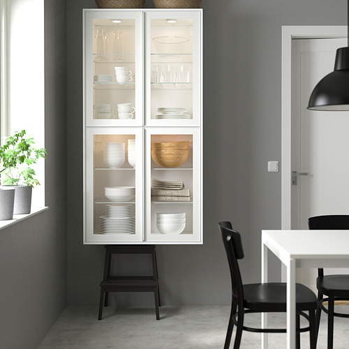 Moderno mueble con puerta de cristal HEJSTA con platos blancos, sillas negras y mesa de comedor.