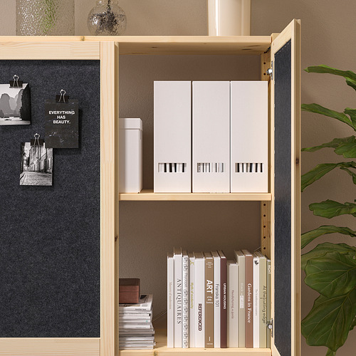 Un mueble de almacenamiento IVAR de madera con puertas con respaldo de fieltro. Tiene cajas blancas y libros, con una cita en una puerta.