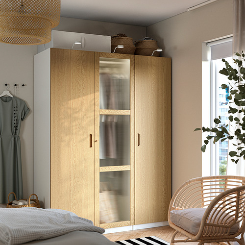 Armario PAX en dormitorio con puerta de cristal, cestas, silla de mimbre, luz natural.