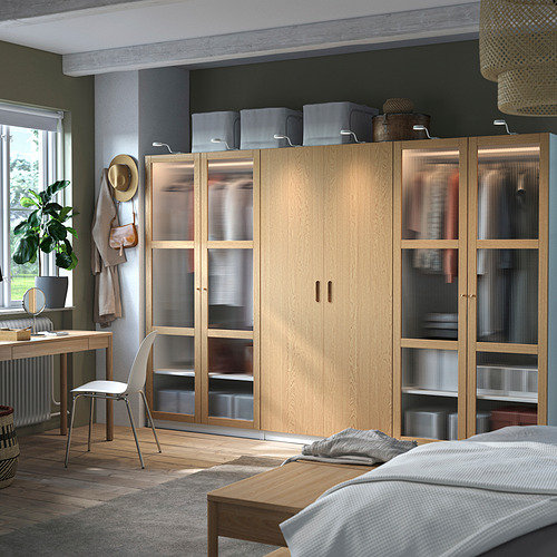 Dormitorio moderno con armario PAX de madera clara, más grande que una silla, con puertas de vidrio y manijas transparentes.