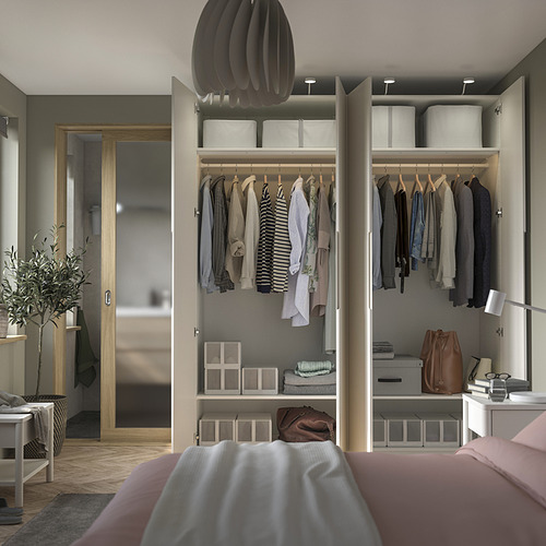 Dormitorio moderno con armario abierto PAX que exhibe ropa, bolsos y cajas de almacenamiento. Una acogedora cama con sábanas rosas está en primer plano.
