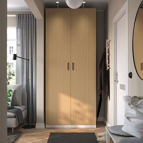 Moderno armario alto de madera TONSTAD en roble beige, entre ventana y puerta, con tiradores lisos.