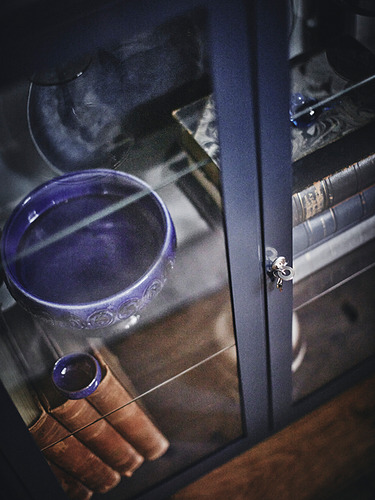 Armario con puerta de cristal FABRIKÖR con plato, llaves y libros azules, con estantes ajustables y cerradura de puerta con llaves metálicas.