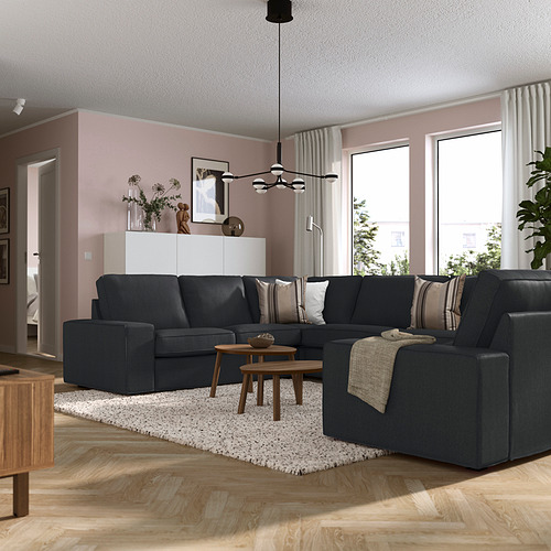 Sala de estar moderna con sofá gris KIVIK, mesas de madera, paredes rosas, grandes ventanales y cortinas blancas.