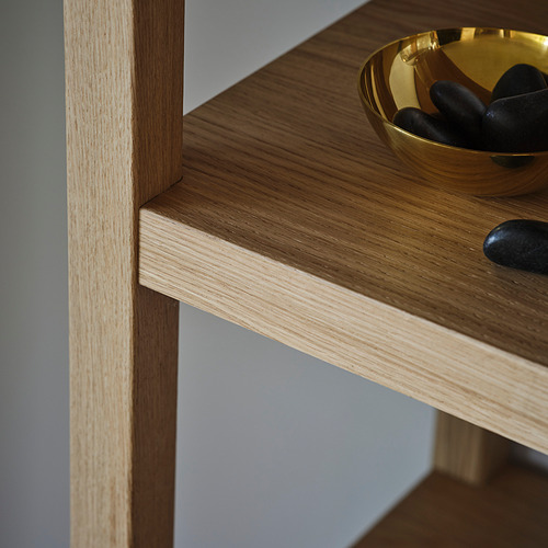 Estante de roble bien elaborado con chapa lisa, que muestra vetas naturales. El cuenco dorado con guijarros negros se encuentra elegantemente en un estante ancho.