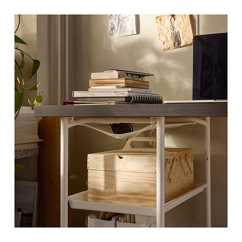 Un escritorio LAGKAPTEN con tapa gris y patas blancas, que contiene libros, un ordenador portátil y cajas de almacenamiento.