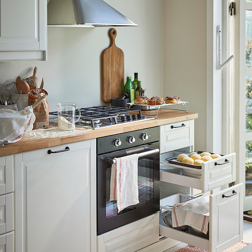 Cocina con electrodomésticos ligeros de encimera, utensilios y una estufa con alimentos expuestos en una rejilla para enfriar.