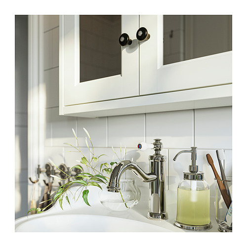 Baño moderno con grifería cromada, dispensador de jabón y planta en burbuja de vidrio. Salpicadero de azulejos blancos y gabinete con perillas negras.