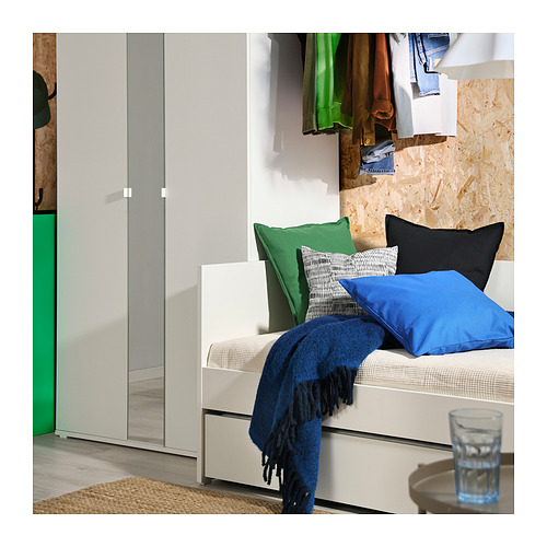 Moderno sofá cama blanco con manta azul, almohadas, junto al armario.