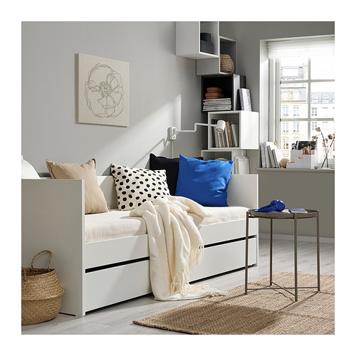 Acogedor dormitorio con sofá cama blanco, almohadas azules y negras, estantería y vista a la ventana.