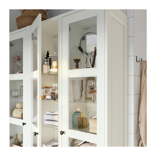 Armario blanco con puertas de cristal, que muestra objetos cuidadosamente dispuestos como frascos, botellas y toallas.